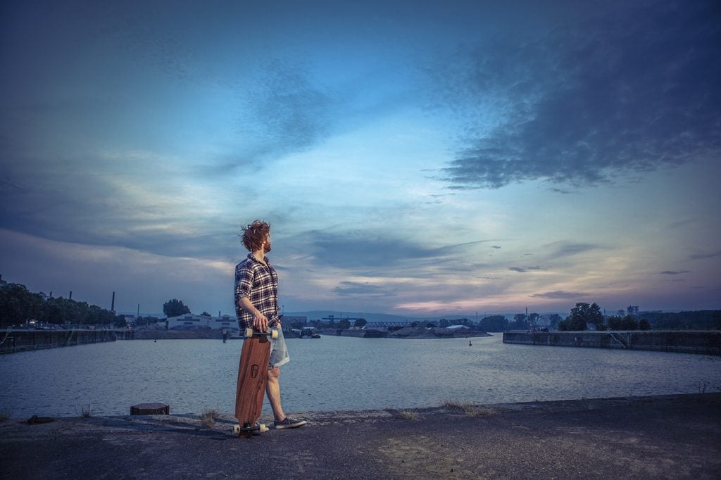 Frau mit Rucksack am Flussufer bei Sonnenuntergang in Köln, professionelle Fotografie.