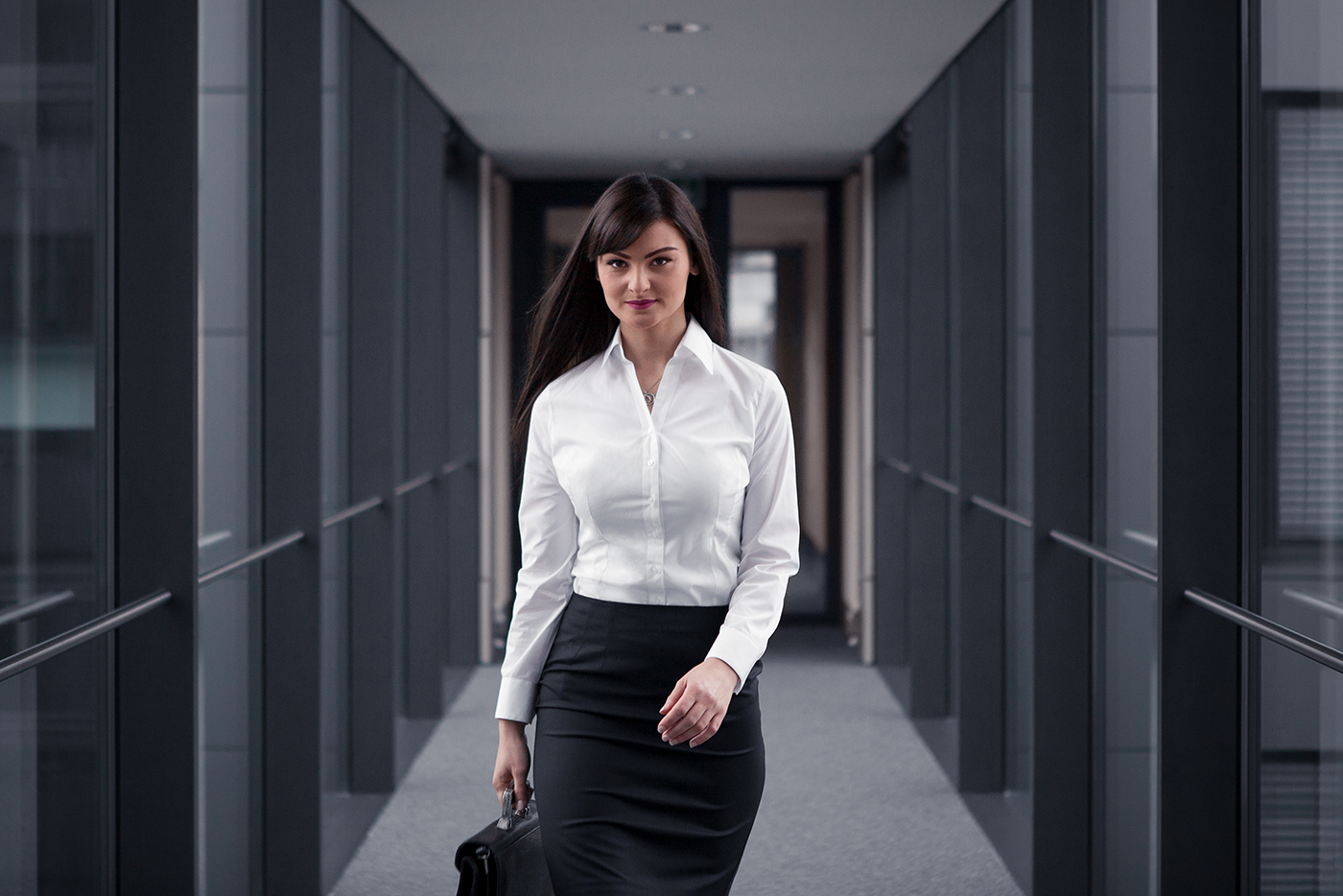 Junge Businessfrau in weißer Bluse und Bleistiftrock geht selbstbewusst durch einen modernen Büroflur