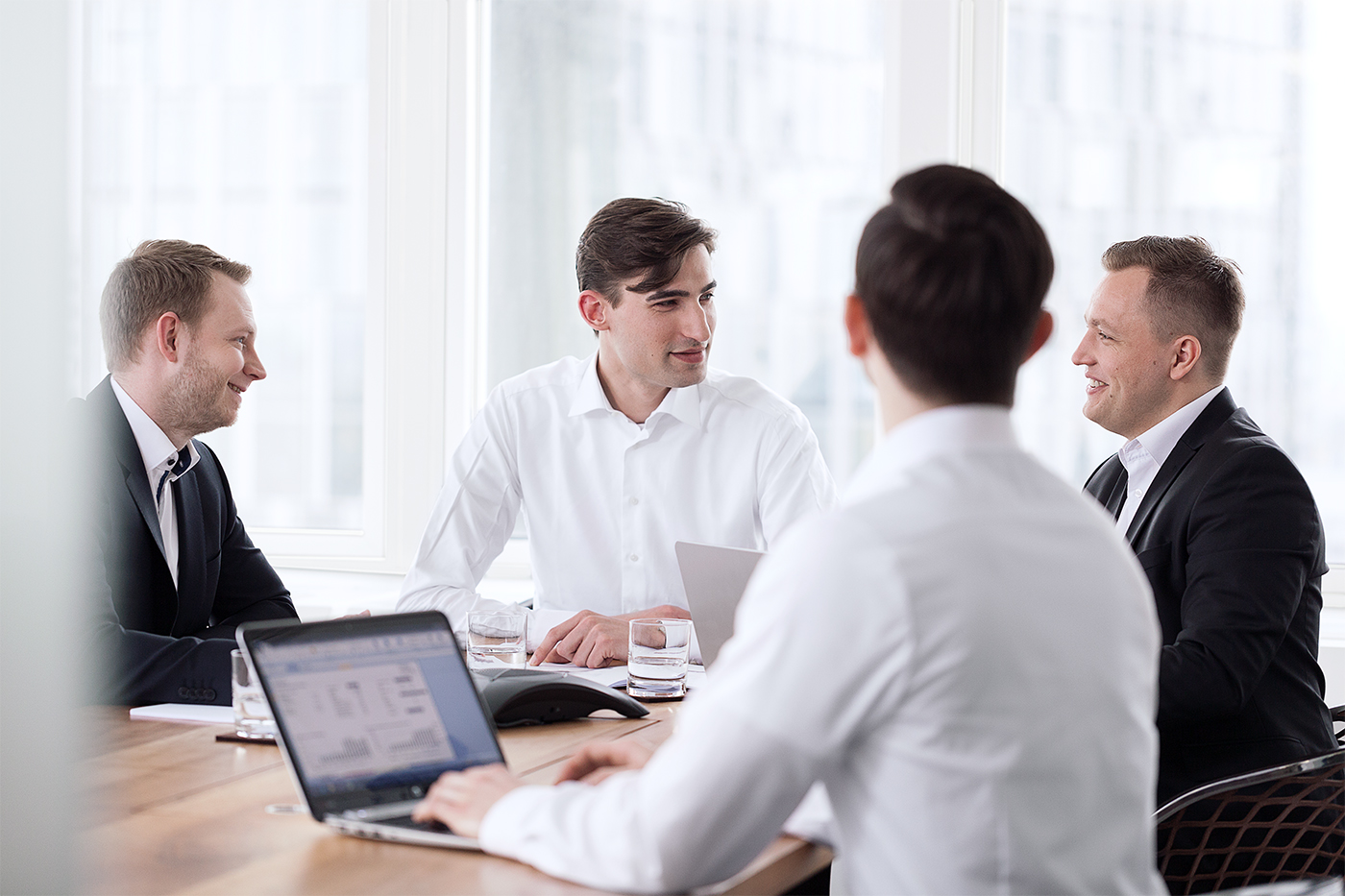 Teamfoto eines Businessmeetings in einem hellen Konferenzraum mit Laptops und Arbeitsmaterialien