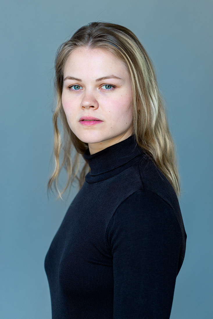 Junge Frau im schwarzen Rollkragenpullover mit Schulterblick vor neutralem Hintergrund – professionelles Porträtfoto für Schauspielerin und Business-Profile