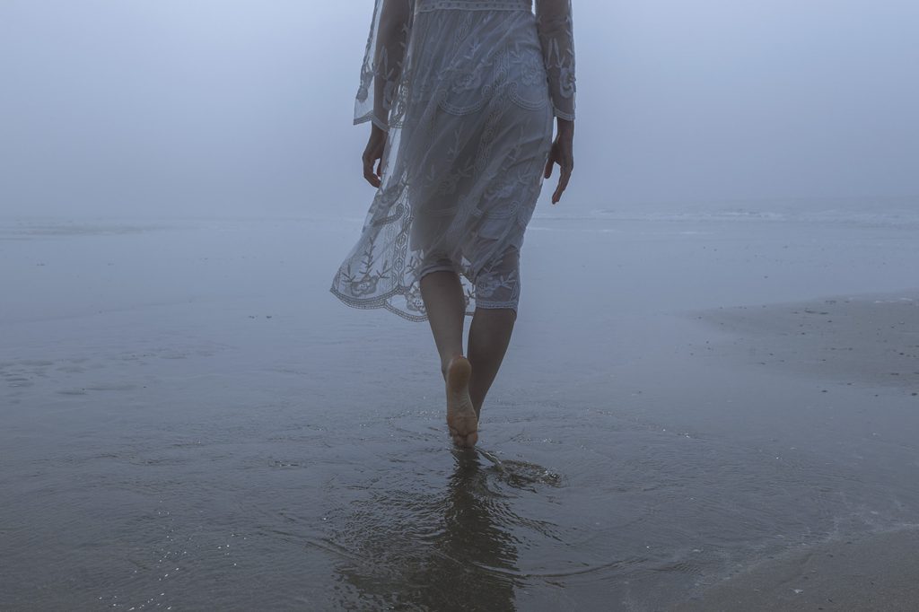 Frau läuft barfuß am Strand bei Nebel, kreative People-Fotografie.